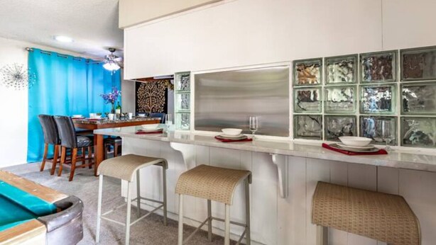 Une cuisine moderne avec un coin bar, des meubles blancs et un rideau bleu.