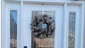 Une porte blanche à deux battants, ornée d’une guirlande décorative, dotée d’un clavier pour l’ouverture et d’un panneau en verre avec un motif géométrique.