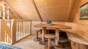Un interior de madera con techo alto, una mesa de madera con taburetes y un cuadro en la pared.