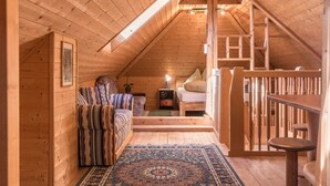 Un interior de madera con una cama tipo litera, un sofá, una mesita y una escalera.