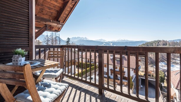 Una terraza de madera con una mesa y sillas, con vistas a un paisaje montañoso.