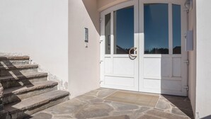 Fachada blanca con puerta curva, escalones de piedra y un pequeño espacio exterior.