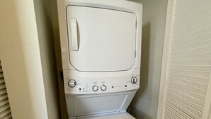 A compact, white laundry room with a built-in washer and dryer, featuring control knobs and a small shelf. - Modern studio fully equipped (Doral)