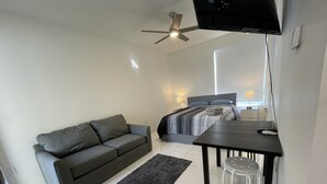 A modern bedroom with a grey sofa, a bed with grey bedding, a small table, and a ceiling fan. - Modern studio fully equipped (Doral)