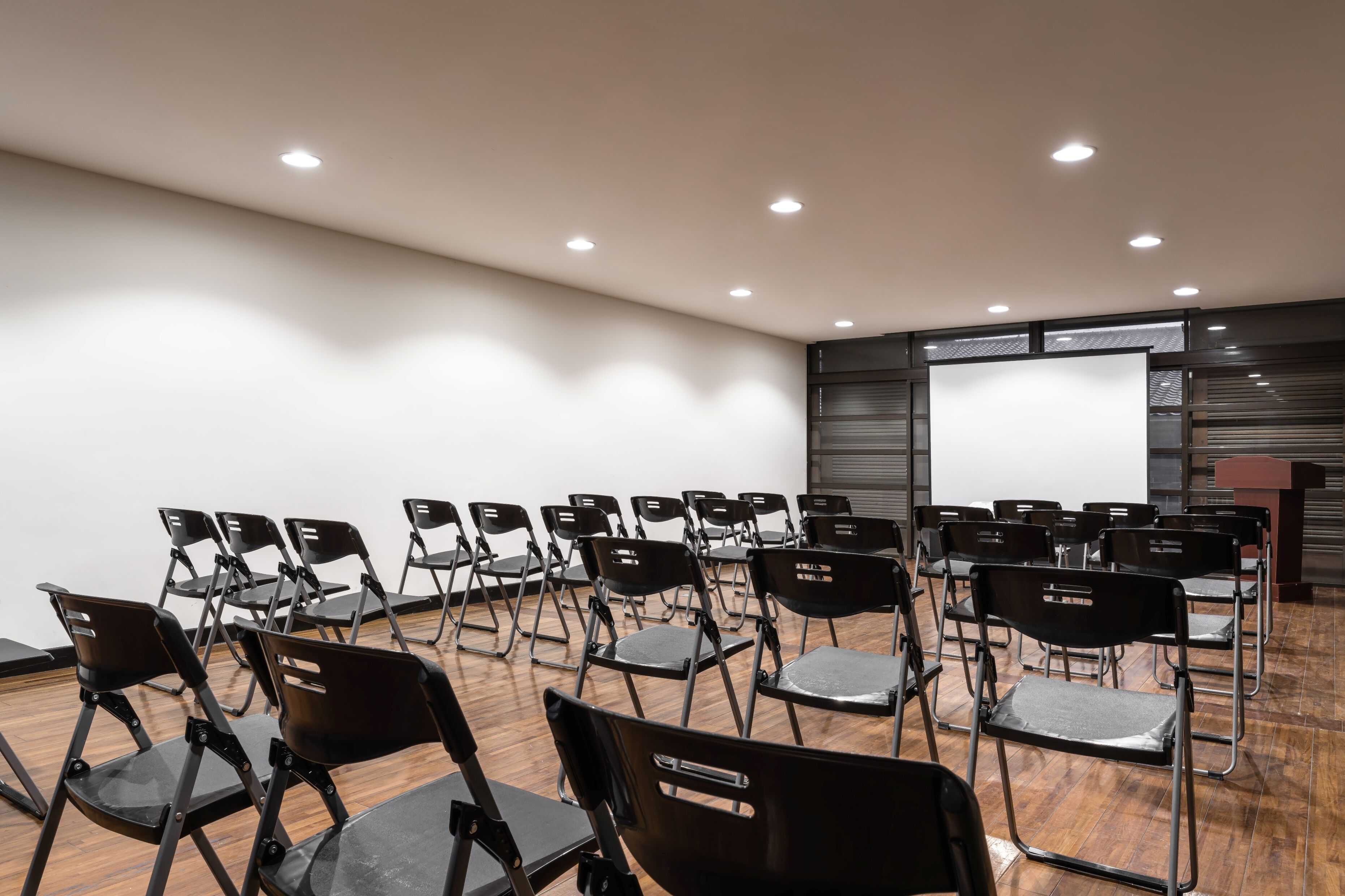 Une salle de conférence avec des rangées de chaises pliantes, un écran de projection et un pupitre.