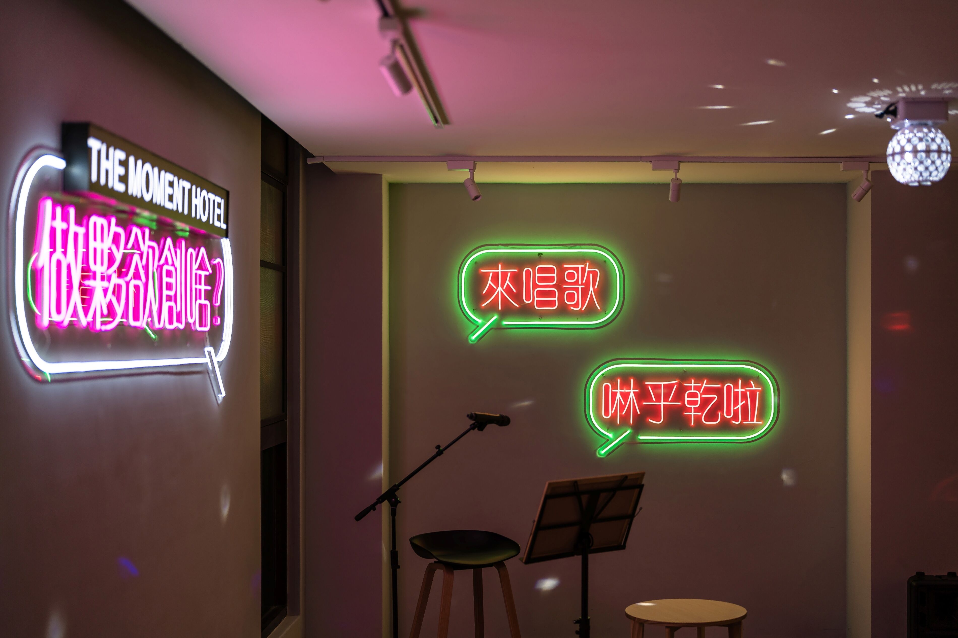 A hotel interior with a neon sign reading "THE MOMENT HOTEL" and two neon speech bubbles with Chinese text.