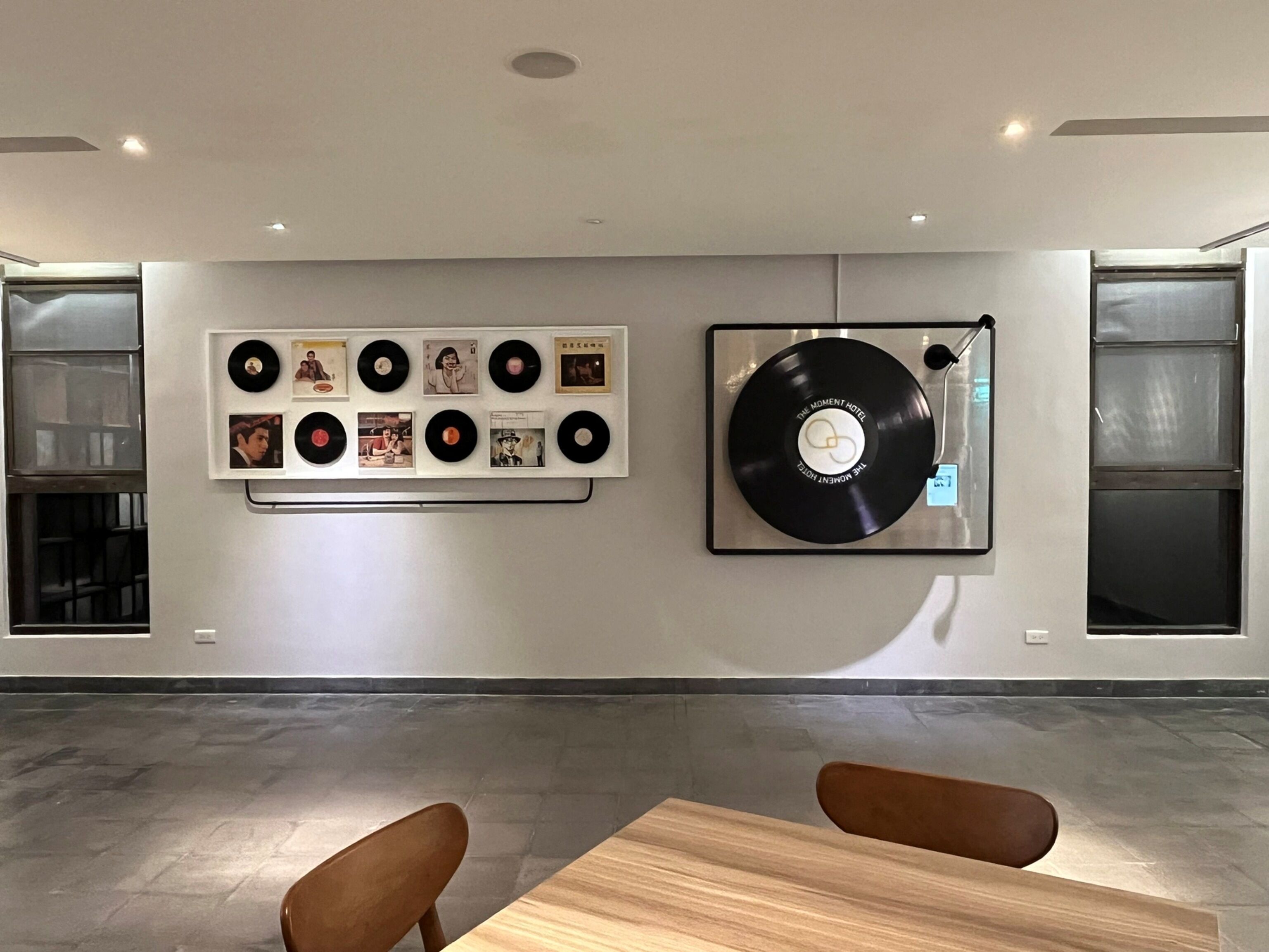 A modern hotel room with a wall-mounted record player and vinyl records, a wooden table, and two brown chairs.