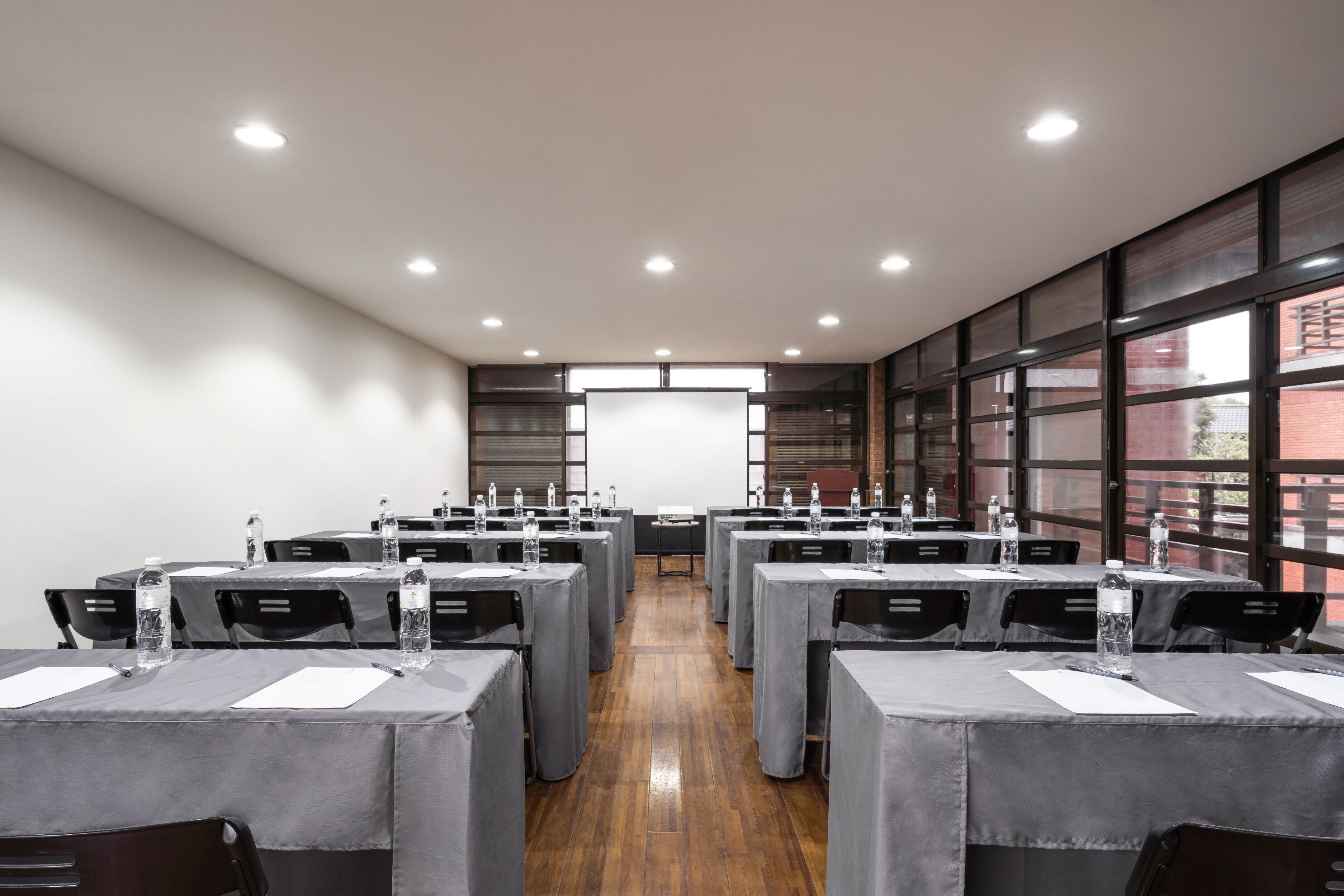 A conference room with multiple tables, each equipped with water bottles and notepads, and large windows on one side.