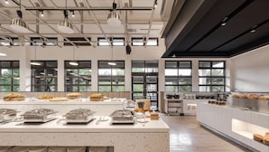 Een moderne buffetopstelling met meerdere bedieningspunten, grote ramen en een ruim, verzorgd interieur.