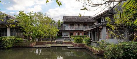 A traditional building with a courtyard and a pond, surrounded by greenery.
