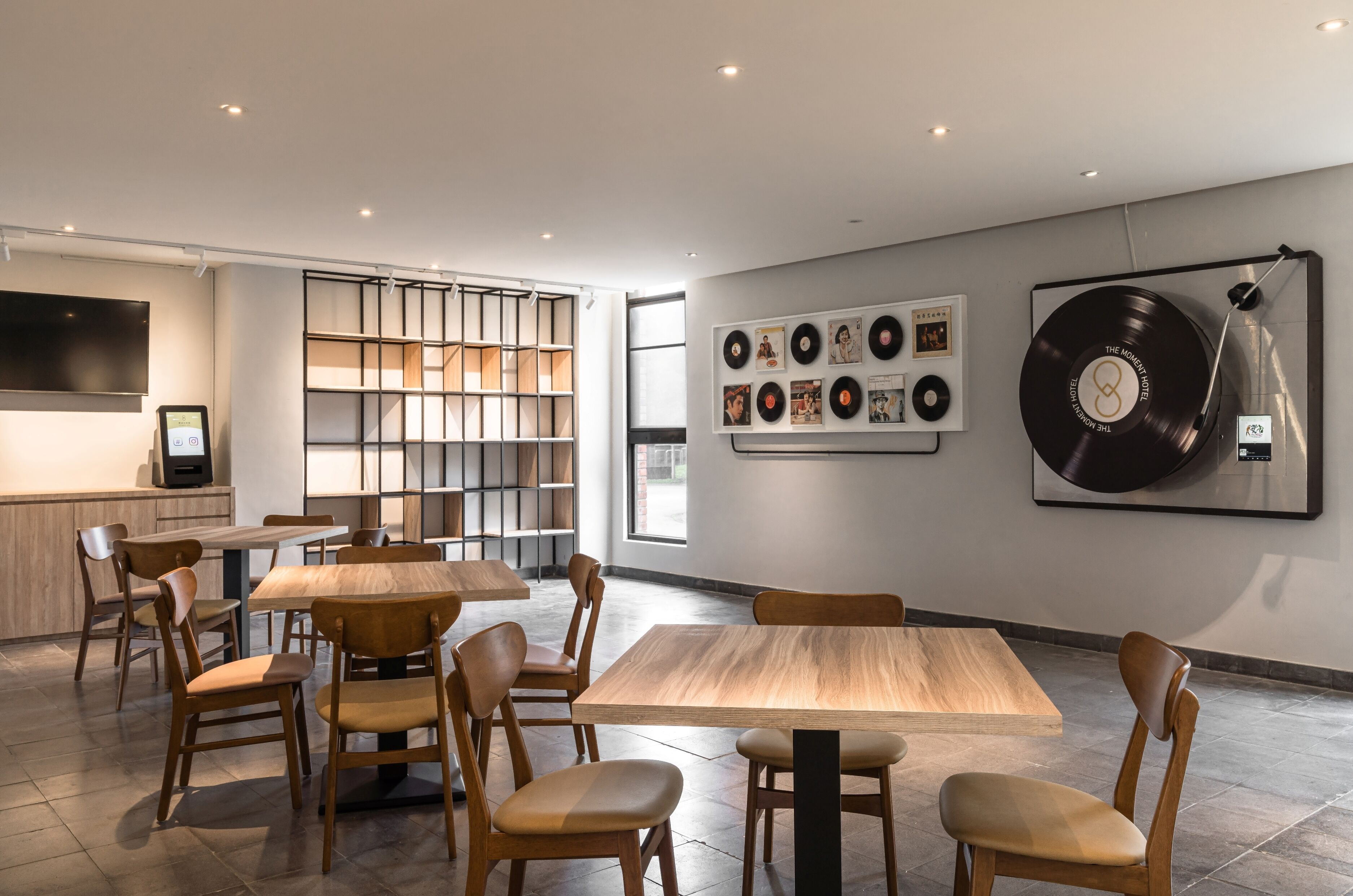 Un comedor moderno con mesas y sillas de madera, un jukebox y una pared decorada con discos de vinilo y fotografías enmarcadas.