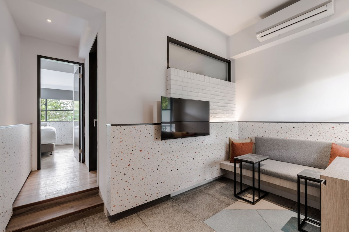 A modern living room with a TV mounted on a white brick wall, a grey sofa with orange cushions, and a small wooden table.