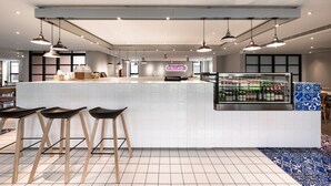 Een moderne bar met een witte betegelde toonbank, drie zwarte barstoelen, hangende吊灯 en een koelvitrine met drank.