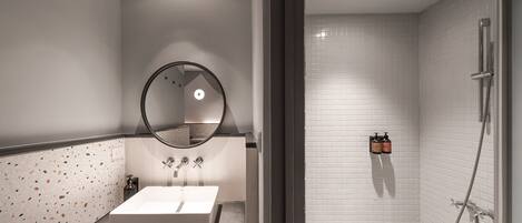 A modern bathroom with a white sink, a round mirror, and a shower area with a glass door.