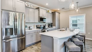 A modern kitchen with stainless steel appliances, a central island with bar stools, and pendant lighting.