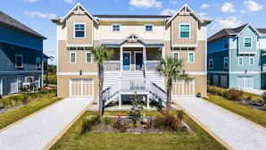 A two-story house with a front porch, a small garden with palm trees, and a driveway.