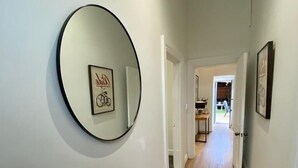 Un couloir avec un grand miroir rond accroché au mur, un tapis à motifs et un chien qui se dirige vers le fond du couloir.