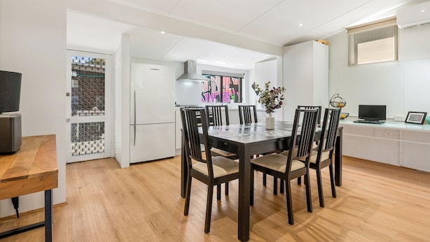 Une cuisine moderne avec des meubles blancs, une table à manger avec des chaises et un téléviseur posé sur un meuble.