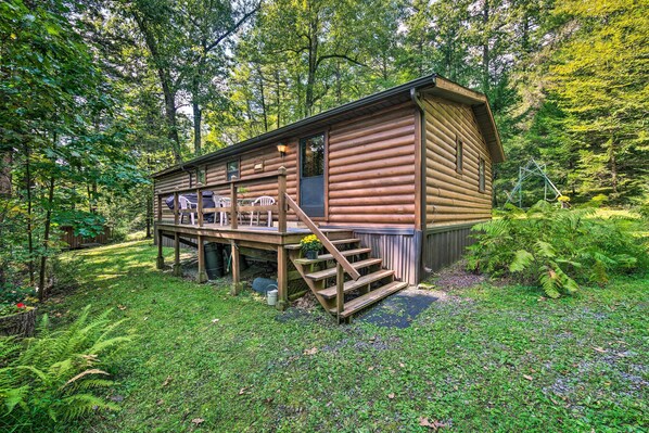Una cabaña de madera con terraza, escalera y un pequeño porche.