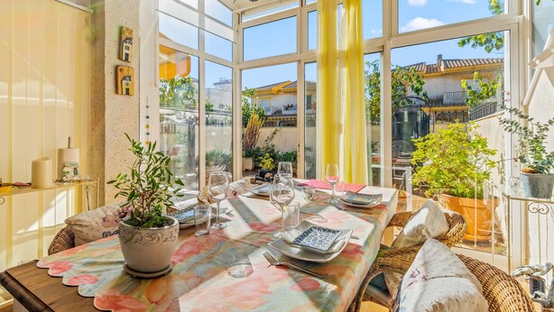 Comedor luminoso con una mesa para dos, ventanas amplias y plantas en macetas.