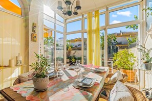 A sunlit dining area with a table set for two, large windows, and potted plants. - Pet-friendly Holiday Home "Seaside House in El Mojon" with Terrace, A/C & Wi-Fi (Pilar de la Horadada)