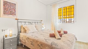 Un dormitorio con una cama, una mesita de noche, una lámpara, una ventana con persianas amarillas y un cuadro colgado en la pared.