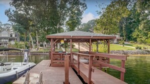A wooden dock with a gazebo, a boat docked at the end, and a house in the background. - Lake Escape - Beautiful Lake Views! - Hot Tub - Game Room - Kayaks - Dock - Firepit - Pet Friendly (Sherrills Ford)