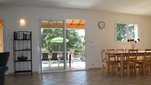 A spacious living area with a sliding glass door leading to an outdoor patio, a dining table with chairs, a bookshelf, and a clock on the wall. - House / Villa - St genest de beauzon (Saint Genest de Beauzon)
