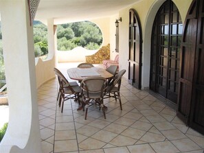 A covered patio with a stone wall, a table with chairs, and a view of greenery. - Villa Bruna with Sea & Mountain View, Garden (Solanas fraz Sinnai)