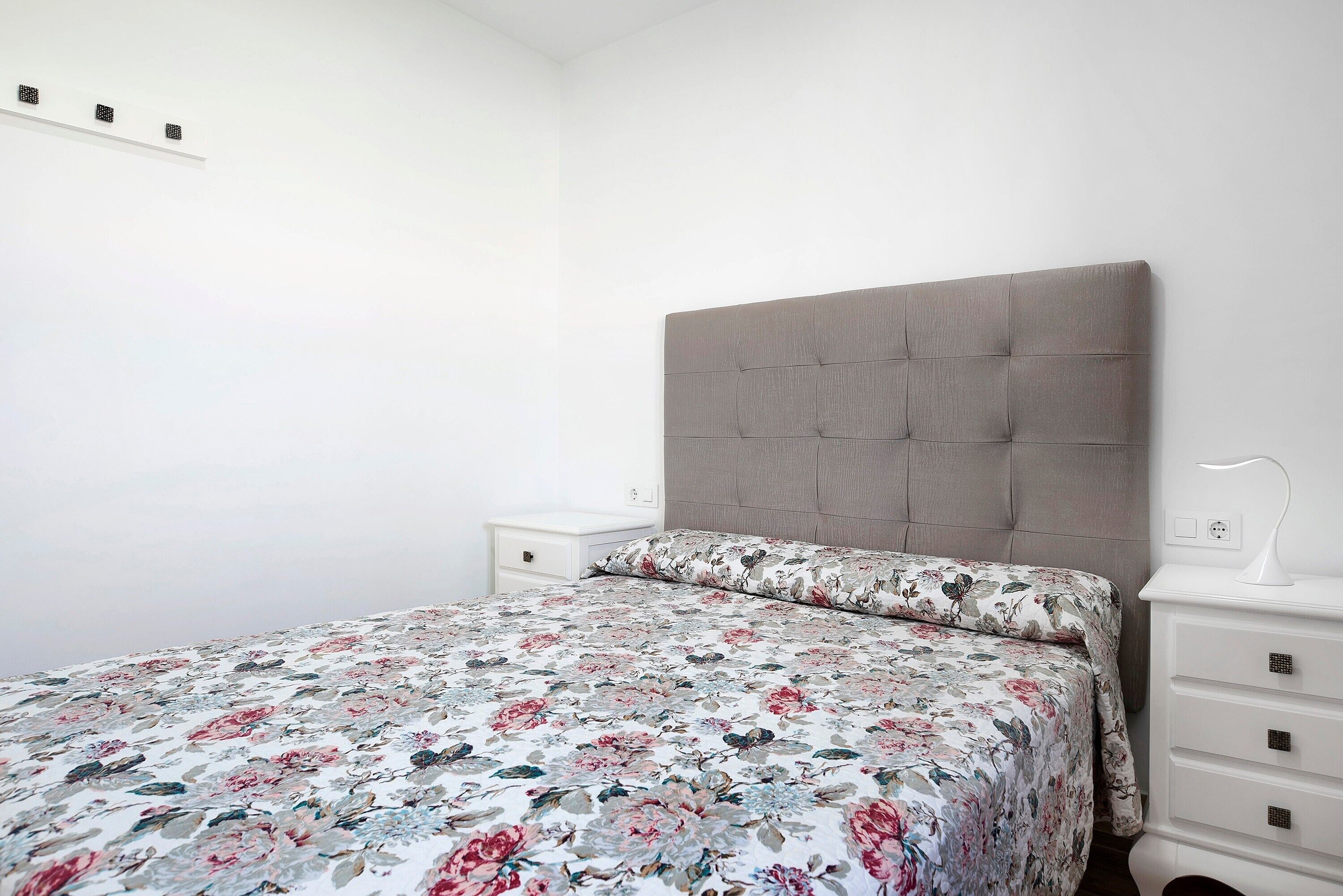 A bedroom with a bed, a nightstand, a dresser, and a wall-mounted light fixture.