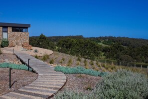Guests can walk along the curved pathway to the entrance, surrounded by native vegetation and rolling hills.