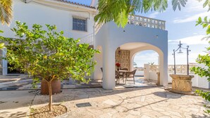 Un patio con piso de piedra, un árbol, un área de descanso y un arco que da a un balcón.