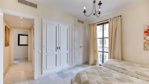 A bedroom with a large wardrobe, a chandelier, and a view through a window with curtains. - Apartment 'Puerto Banus2 Beachfront and Pools' with Shared Pool, Wi-Fi and Air Conditioning (Puerto Banús)