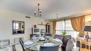 A modern living room with a glass dining table, grey sofas, and a TV in the background. - Apartment 'Puerto Banus2 Beachfront and Pools' with Shared Pool, Wi-Fi and Air Conditioning (Puerto Banús)