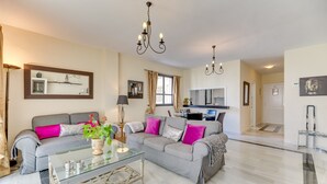 A modern living room with a grey sofa, glass coffee table, and a kitchen in the background. - Apartment 'Puerto Banus2 Beachfront and Pools' with Shared Pool, Wi-Fi and Air Conditioning (Puerto Banús)