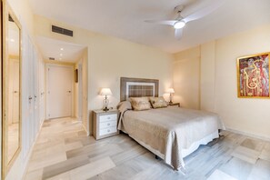 Une chambre à coucher avec un lit, des tables de chevet, un ventilateur de plafond et un tableau accroché au mur.
