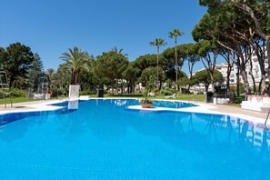 Une piscine d’eau bleue et limpide, entourée d’arbres, avec un bâtiment visible au loin.