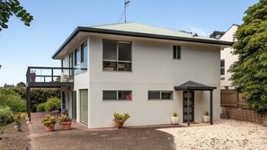 A two-story modern house with a balcony, large windows, and potted plants.
