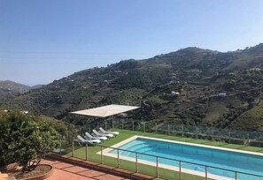 Una piscina con sillones de descanso, una zona de estar cubierta y vistas a viñedos en terrazas.