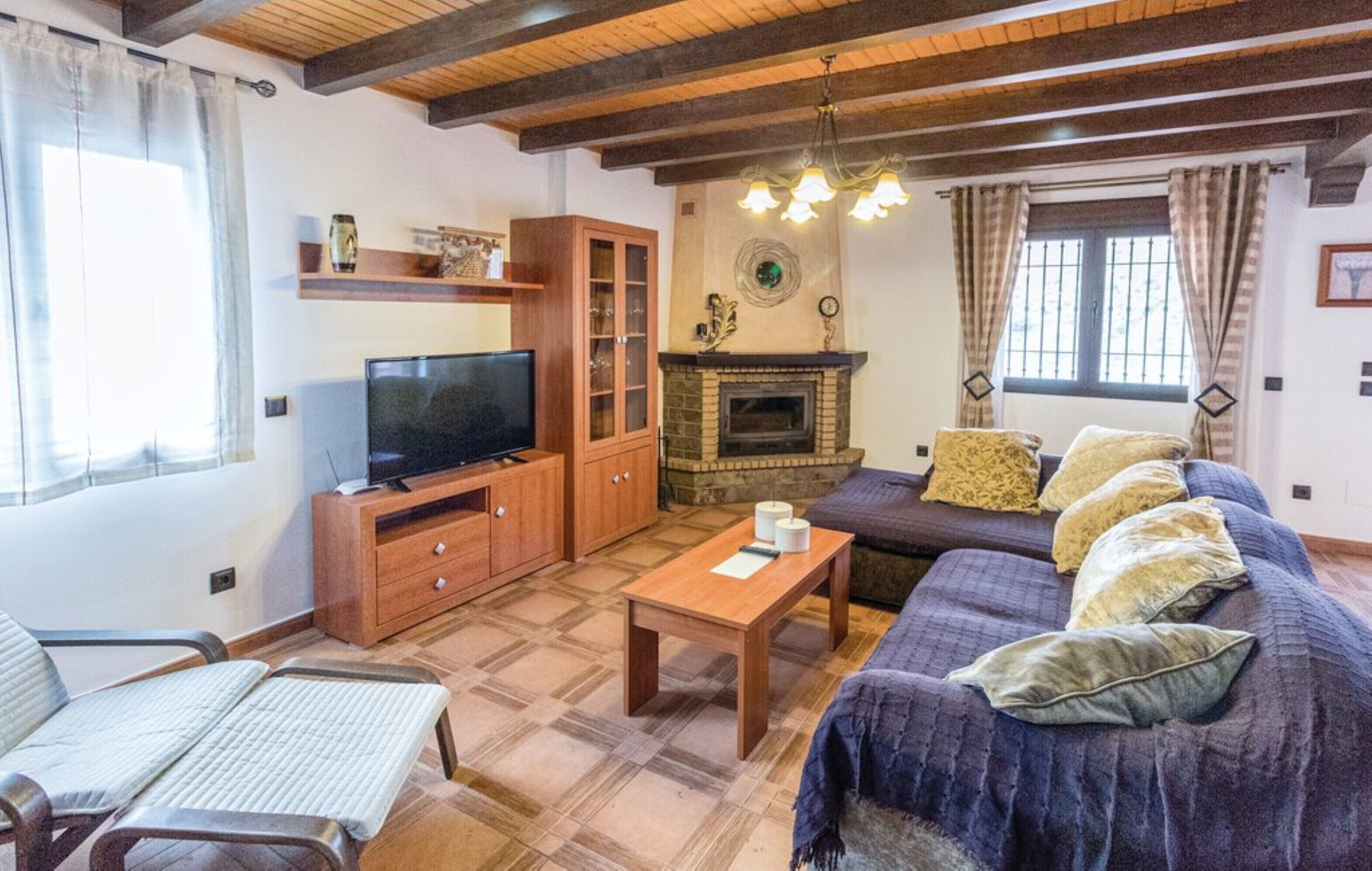 Una sala de estar con televisión, mueble de madera, chimenea, sofá y una ventana con cortinas.