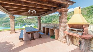 Een terras buiten met een bakstenen barbecue, picknicktafels en uitzicht op heuvels.
