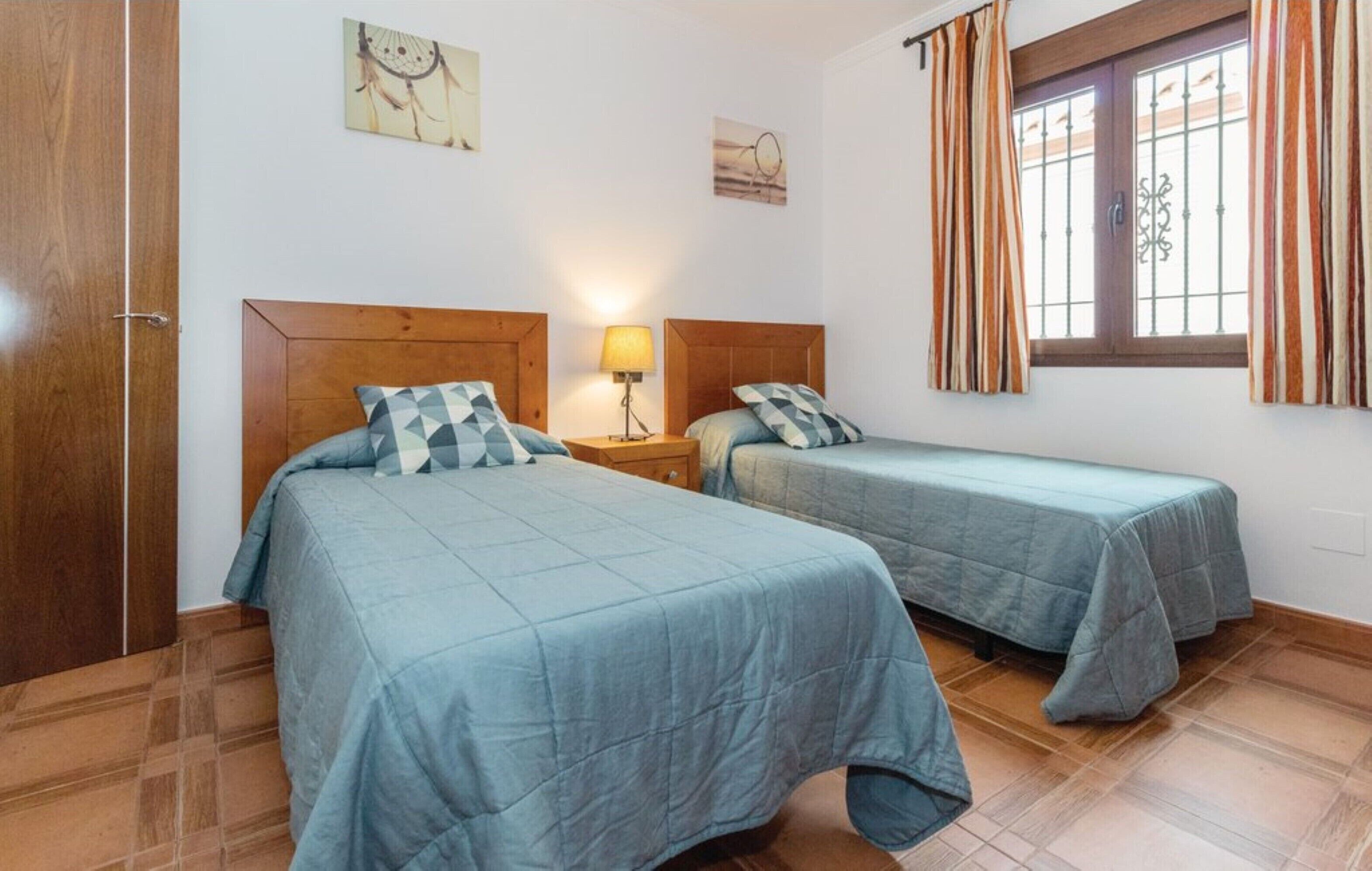 A bedroom with two beds, a wooden wardrobe, and a window with striped curtains.