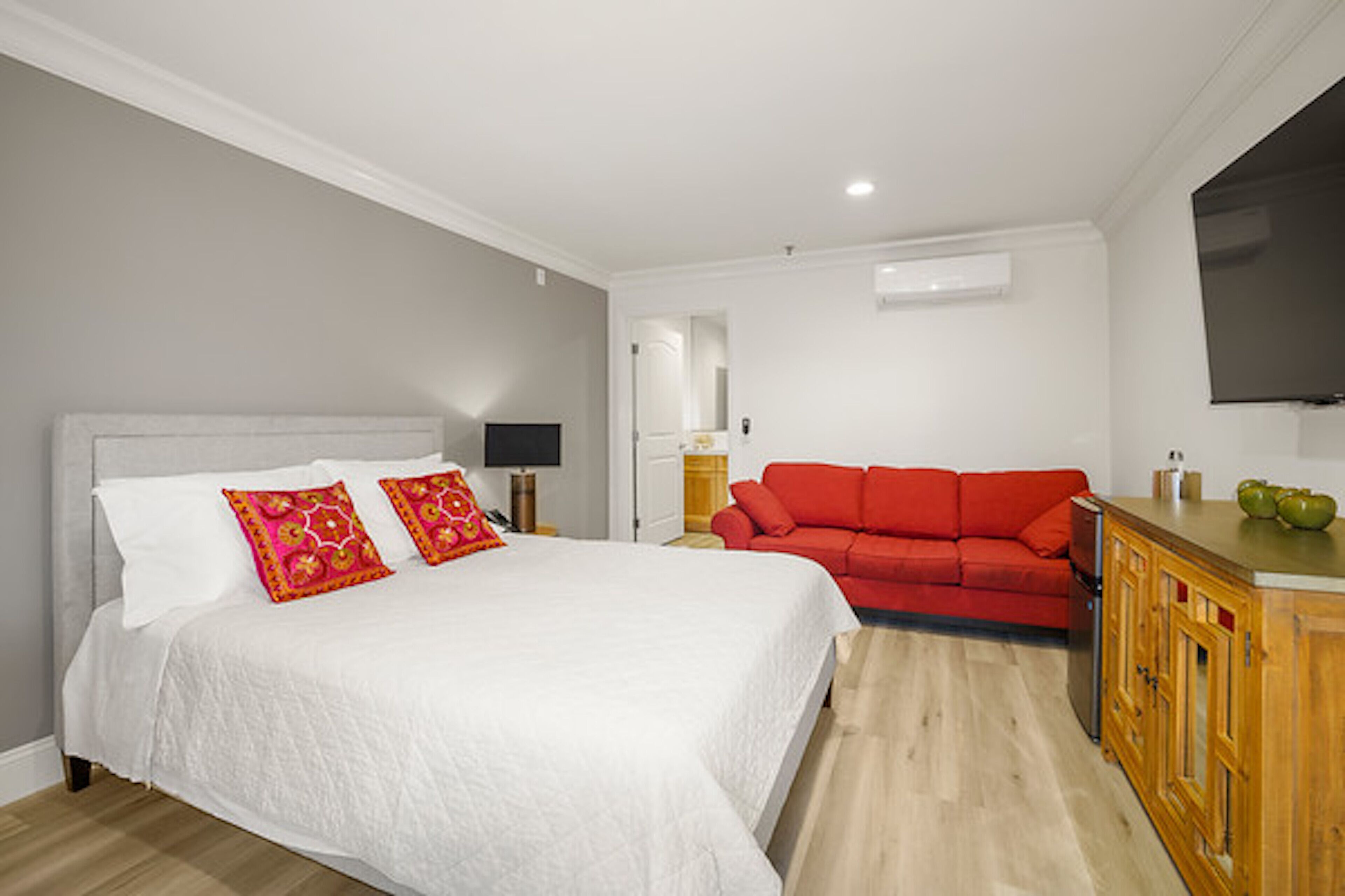 Un dormitorio con una cama, un sofá rojo, un armario de madera y un televisor en la pared.