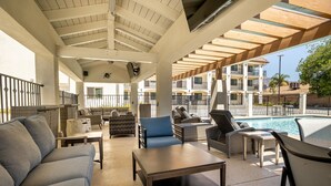 A covered outdoor seating area with sofas, chairs, and a pool in the background. - Hotel Huntington (Duarte)