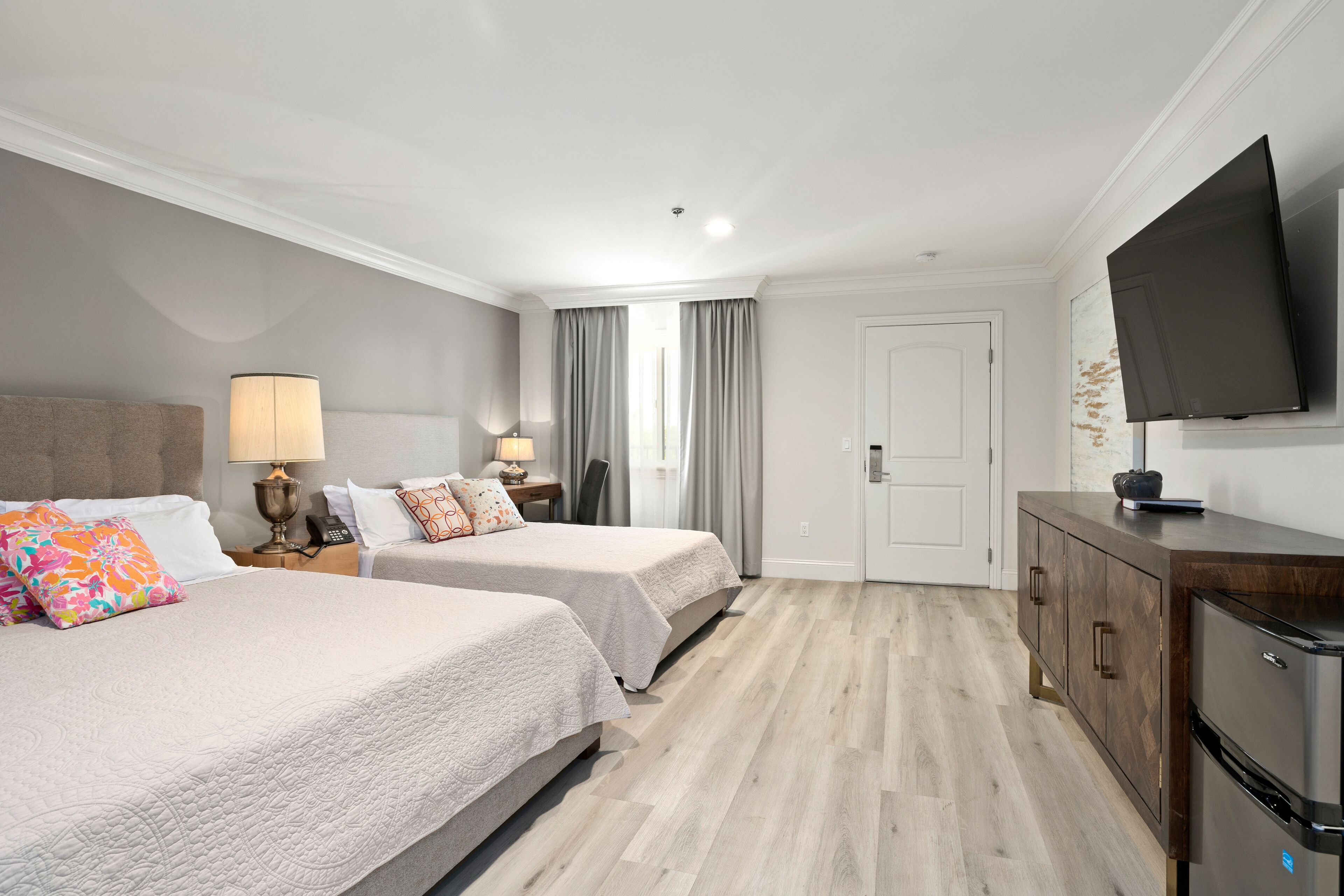 A hotel room with two beds, a TV, a minibar, and a door leading to a bathroom.