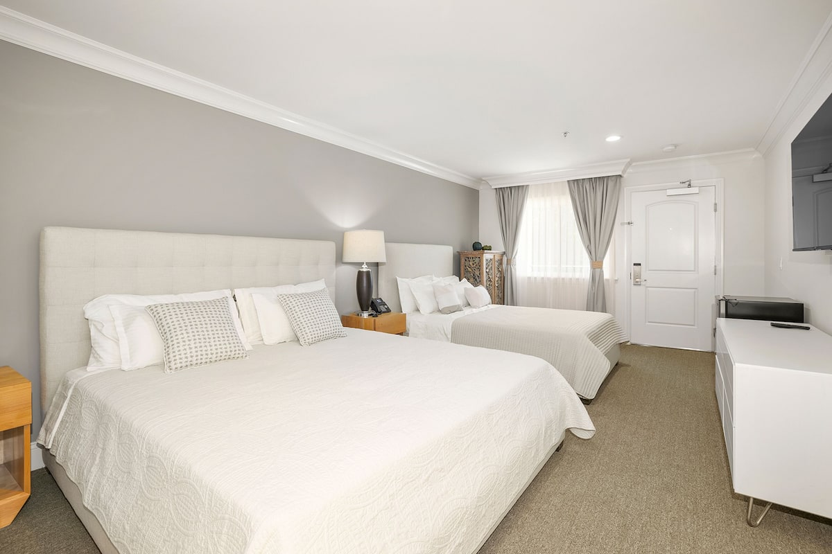 A hotel room with two beds, a desk, a lamp, and a TV.