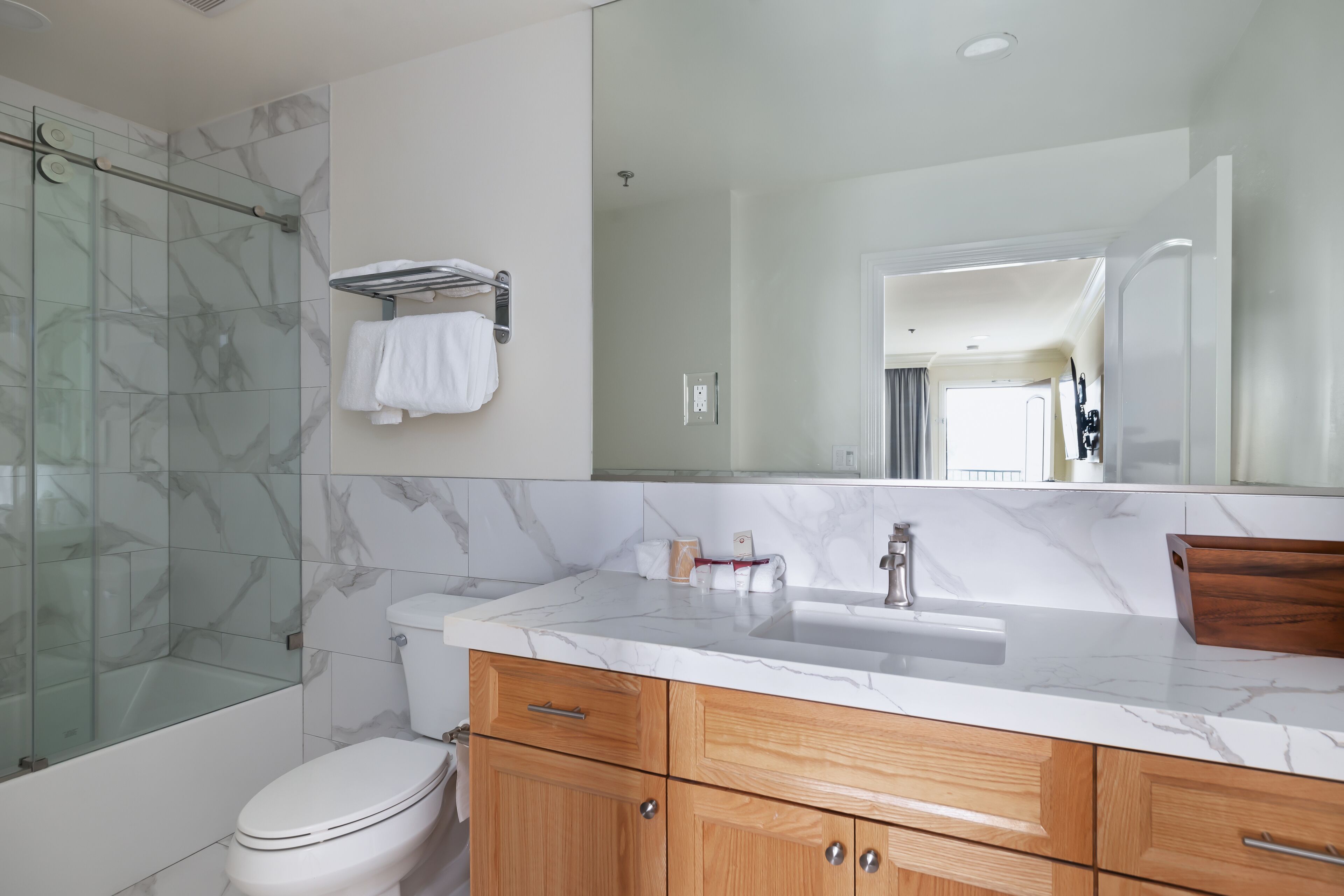A modern bathroom with a glass shower enclosure, a white toilet, a marble sink, wooden cabinets, and a large mirror.