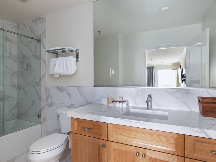 A modern bathroom with a glass shower enclosure, a white toilet, a marble sink, wooden cabinets, and a large mirror.