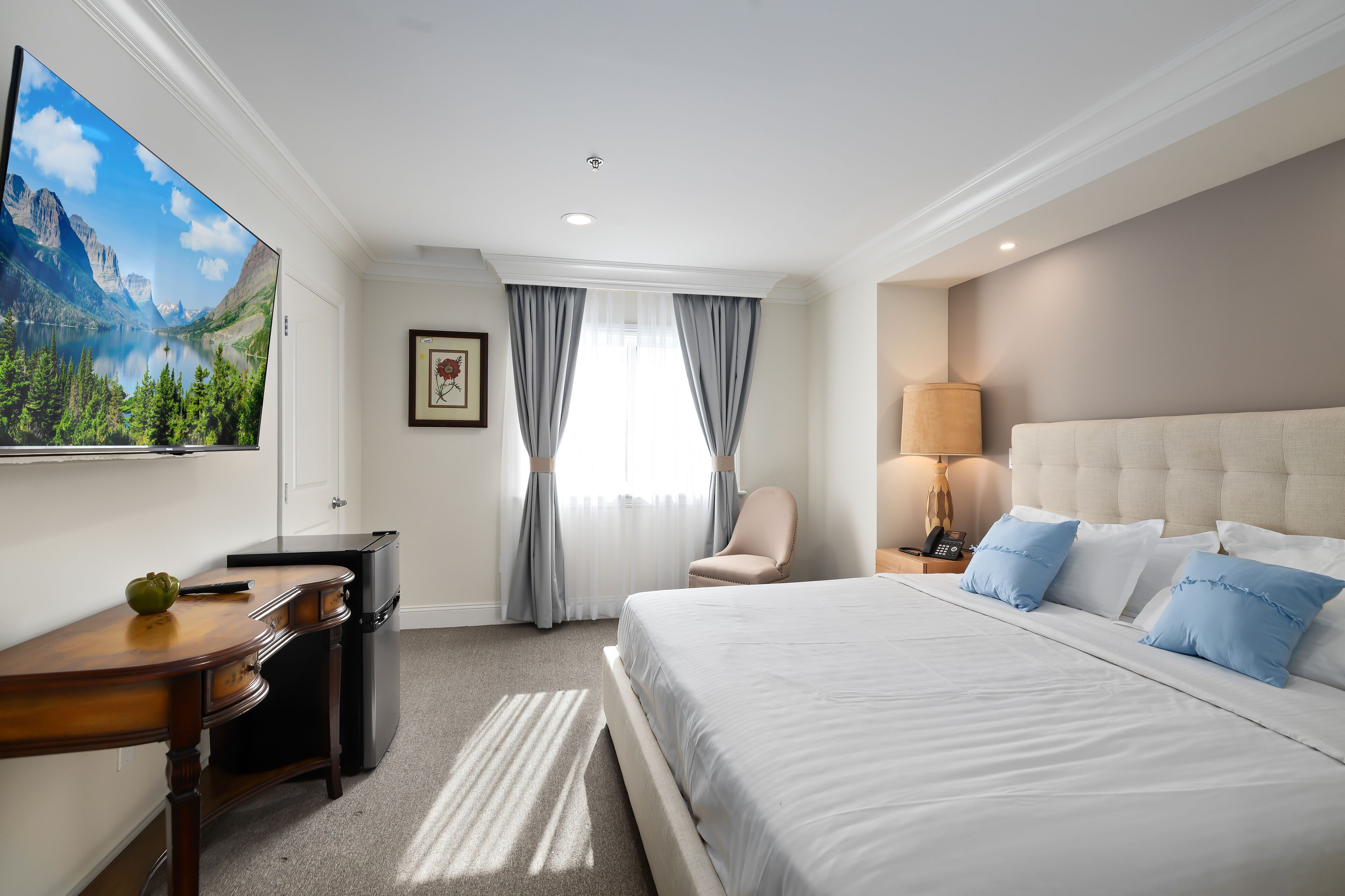 Habitación de hotel con una cama grande, un escritorio con computadora, una silla, un televisor y una ventana con cortinas.