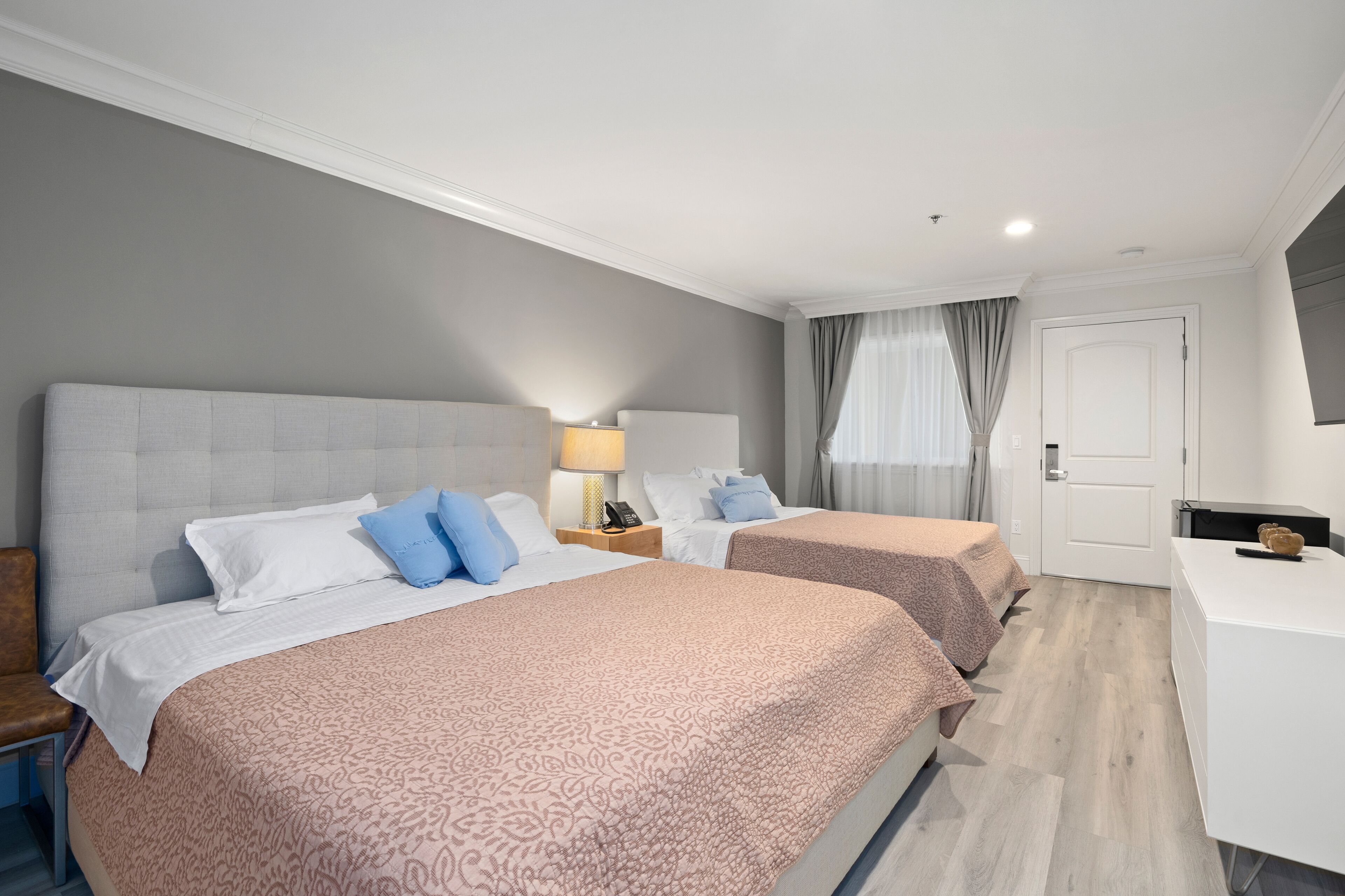 A hotel room with two beds, a desk, a chair, a lamp, and a door.